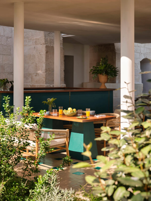 Brightly lit breakfast setting at Bianca Bistrot, featuring a wooden table with drinks, surrounded by greenery and stone a...