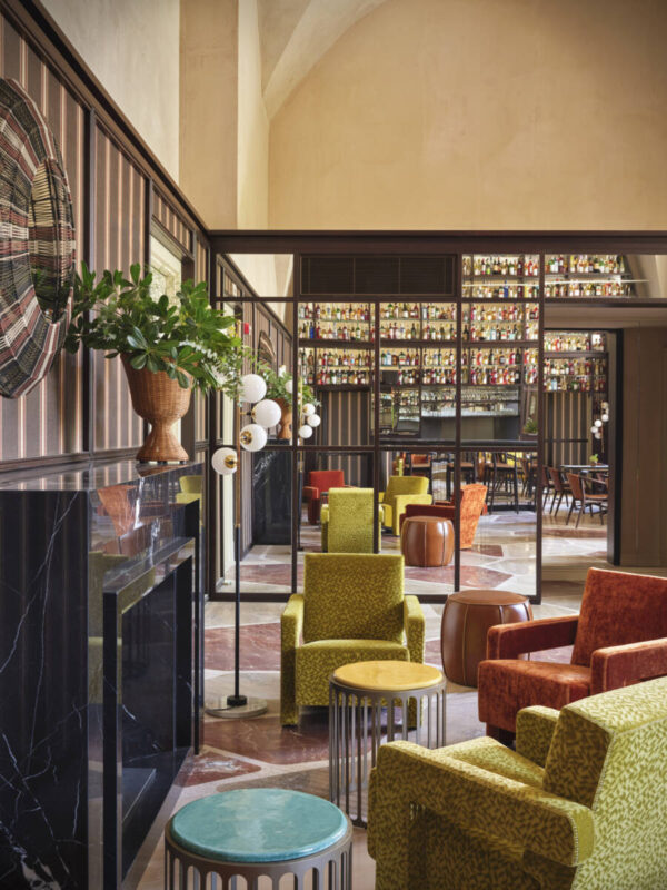 Colorful seating in a stylish lounge with a marble fireplace and a mirrored wall, featuring a bar in the background.
