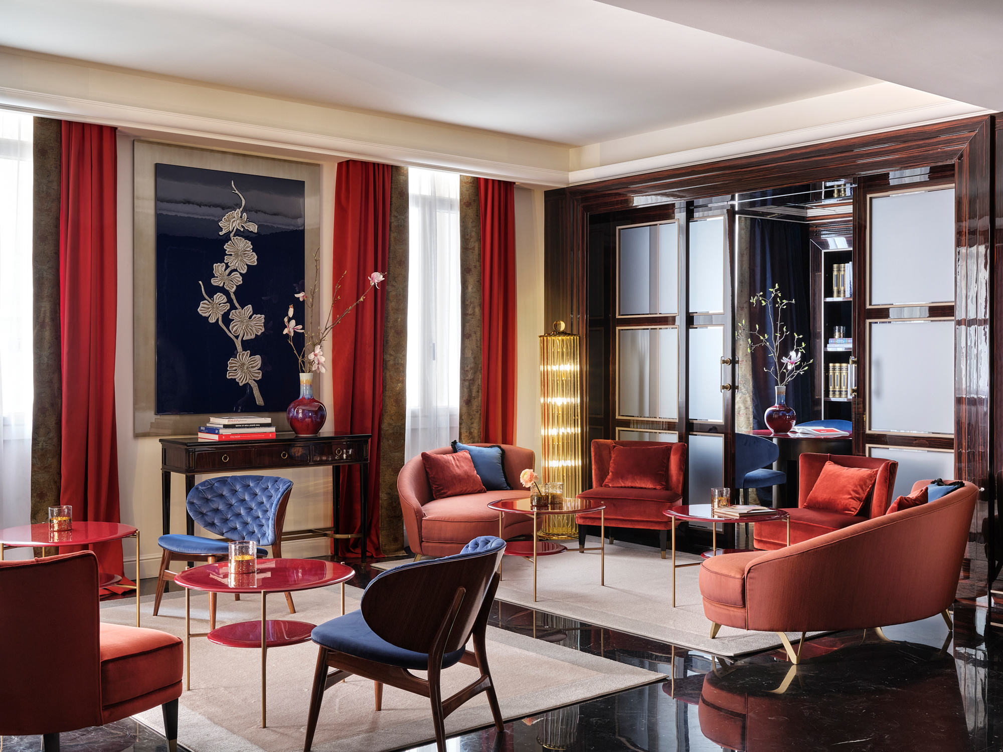 Elegant lounge area with plush seating, red curtains, and decorative artwork, showcasing a modern design aesthetic.