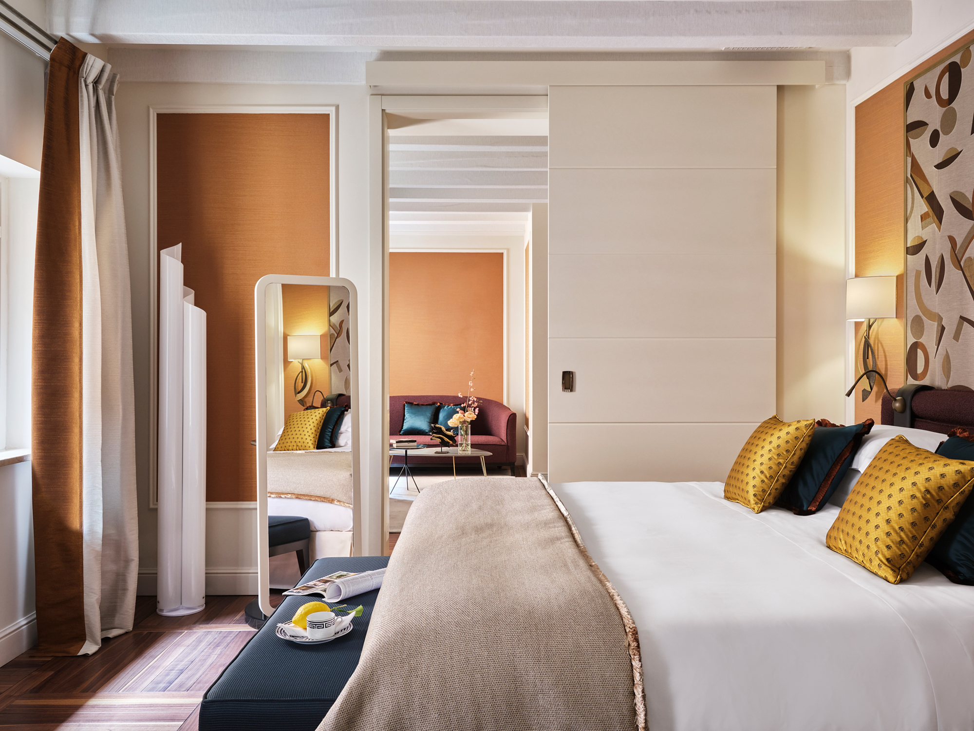 Luxurious hotel room featuring a king-size bed with decorative pillows, a seating area, and elegant decor in warm tones.