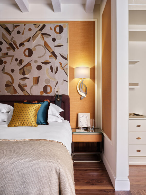 Stylish hotel room featuring a patterned wall, a bed with colorful pillows, and a modern bedside lamp.