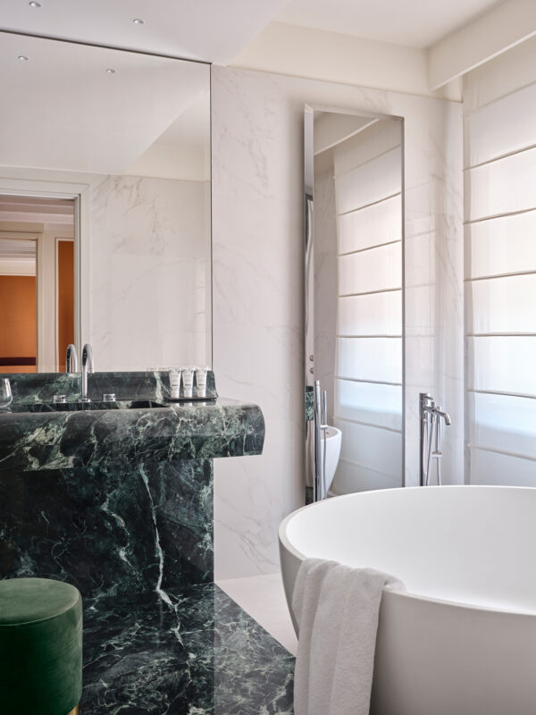 Luxurious bathroom featuring a freestanding white bathtub, dark green marble countertop, and large mirrors.