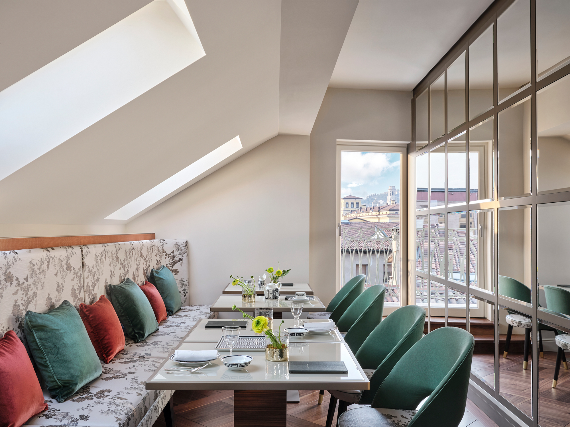 Elegant dining area with a sloped ceiling, featuring a table set with flowers and green chairs, overlooking Verona.