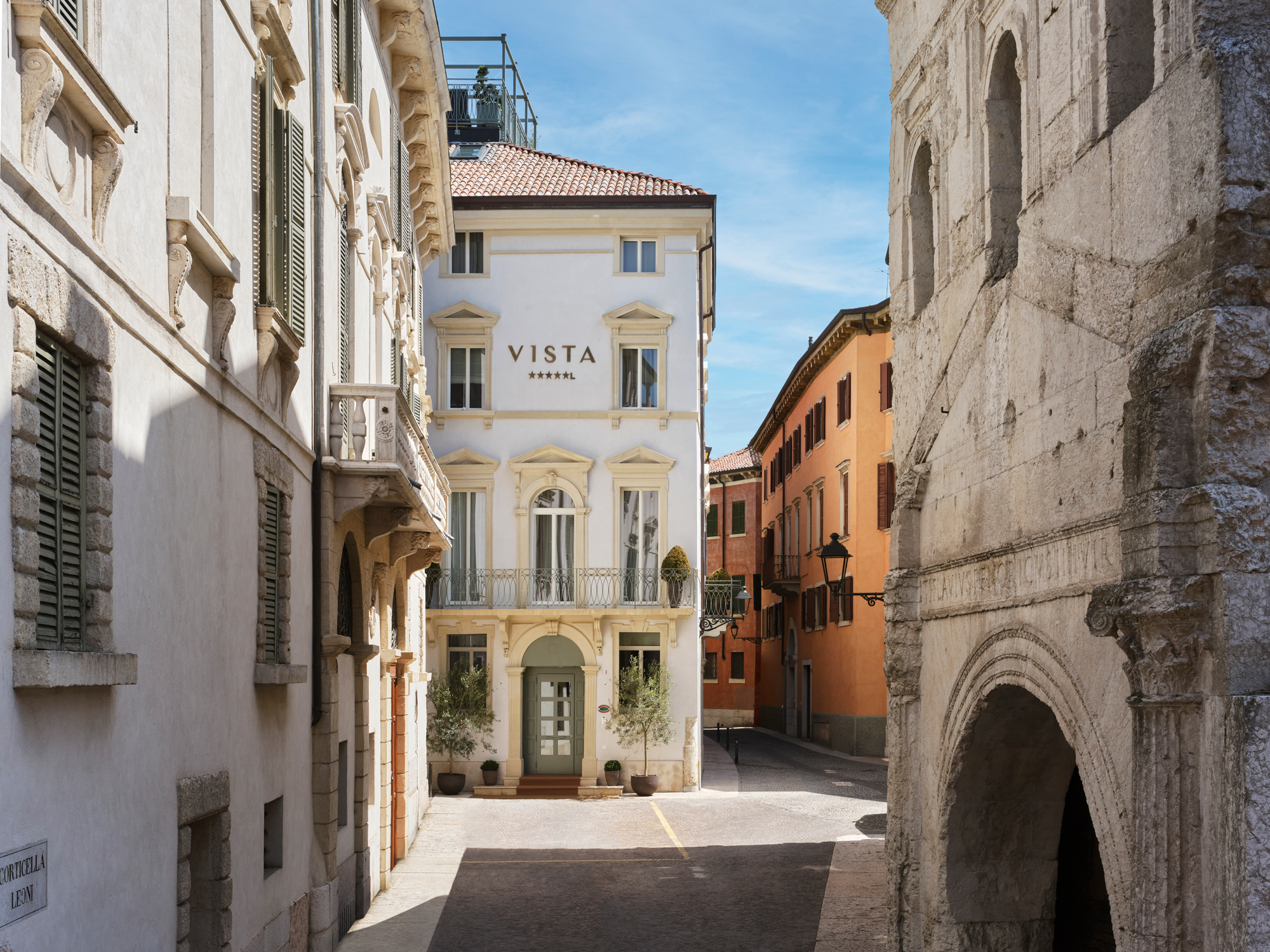 Narrow street in Verona featuring the Vista hotel, surrounded by historic buildings and a clear blue sky.