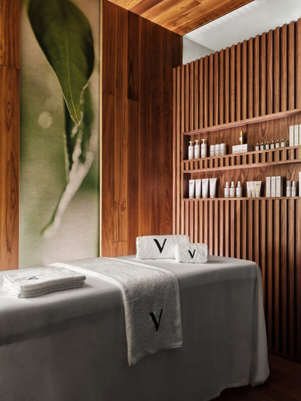 Spa treatment room with wooden walls, a massage table covered in a white cloth, and neatly arranged skincare products on s...