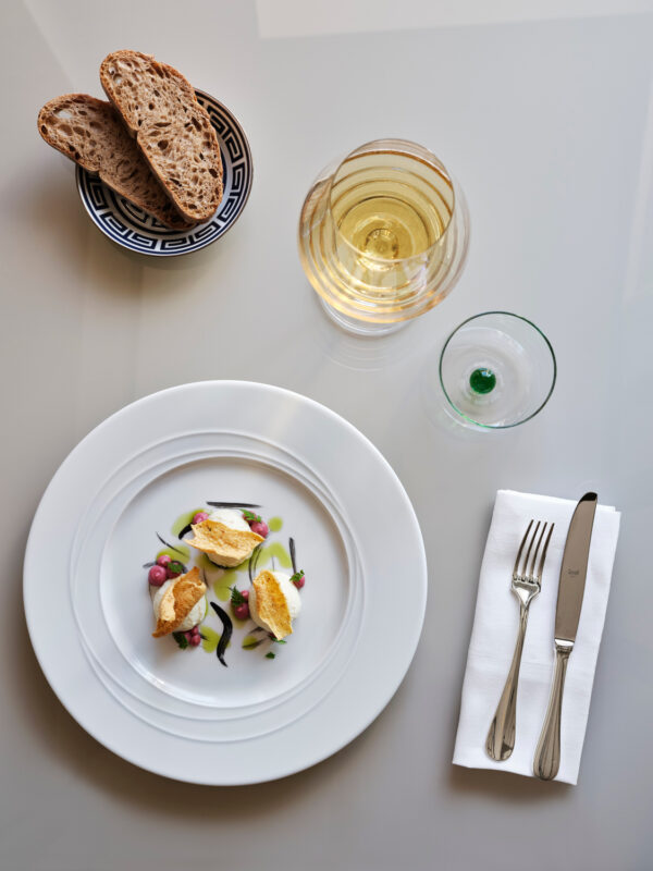 Elegant plate with a gourmet dish, accompanied by a glass of white wine, a water glass, and slices of brown bread.