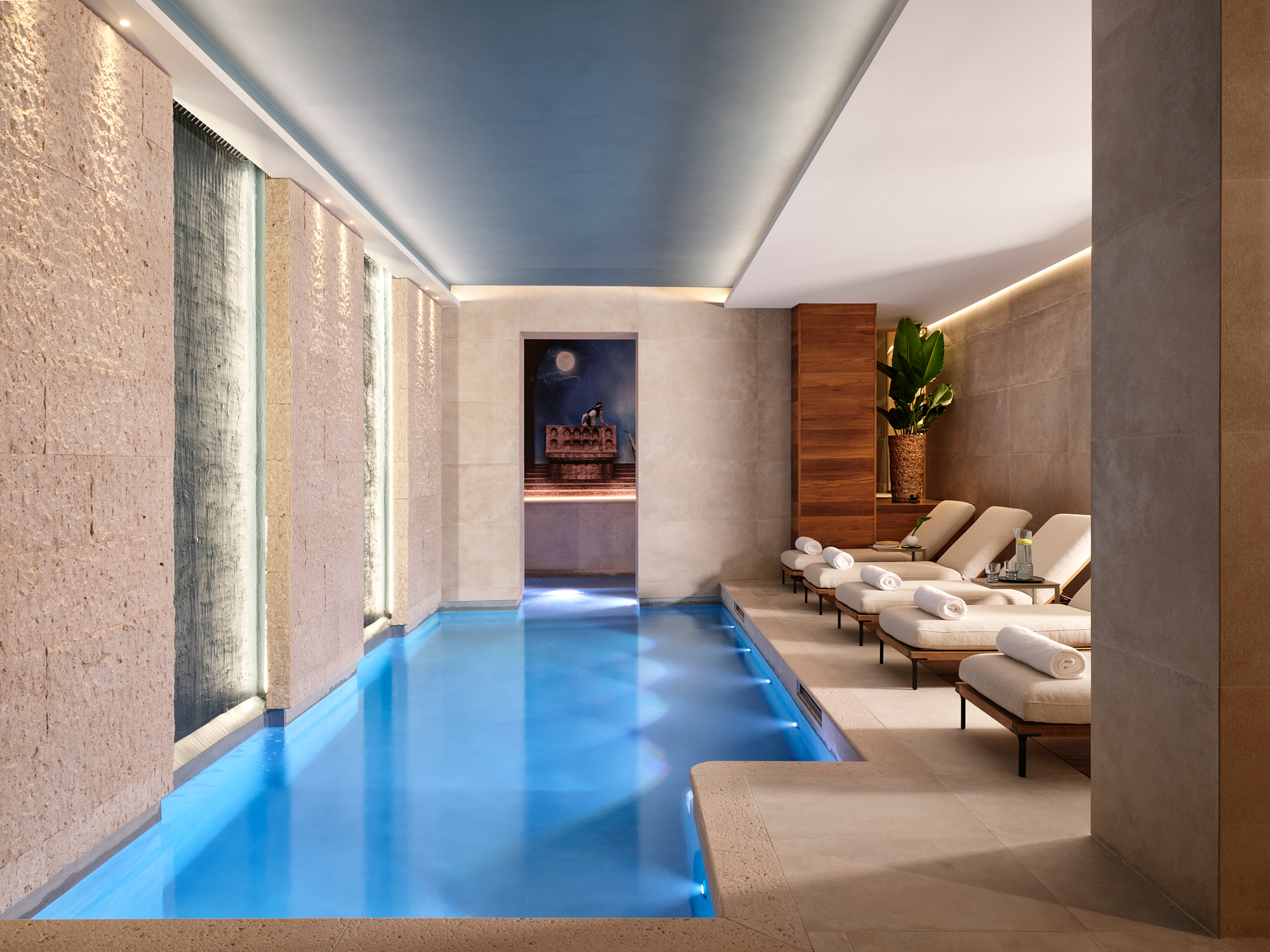 Serene spa interior featuring a tranquil blue pool, lounge chairs, and soft lighting, creating a relaxing atmosphere.