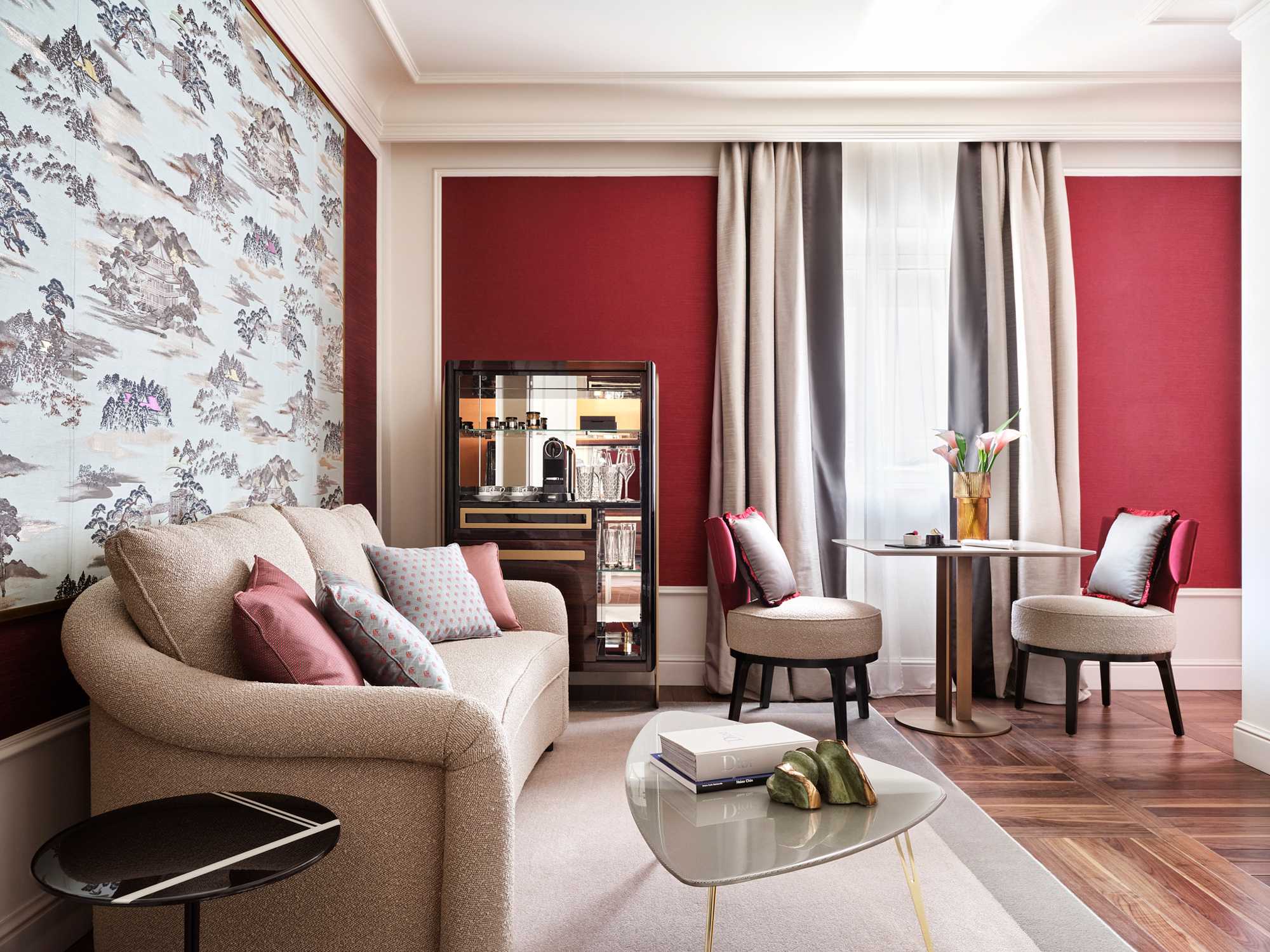 Elegant living area featuring a beige sofa with colorful cushions, a round table, and stylish chairs against a red wall.
