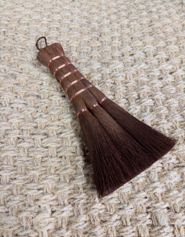 Brown brush with multiple bristles tied together, resting on a textured beige surface.