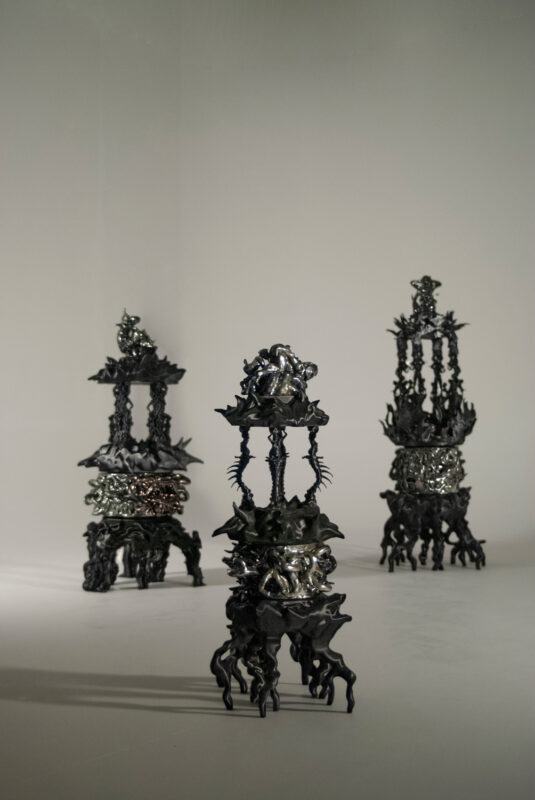 Three intricate black sculptures resembling ornate fountains, featuring detailed figures and decorative elements.