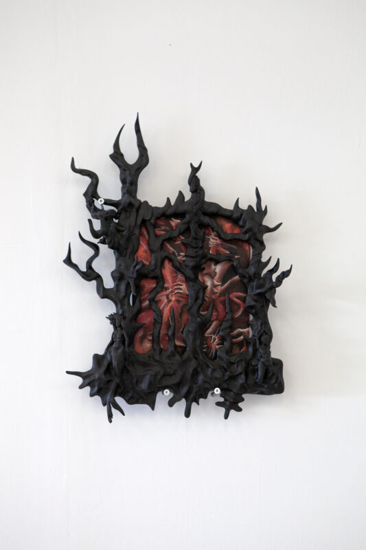 Abstract artwork featuring a dark, textured frame with protruding, twisted forms surrounding a central red and black image...