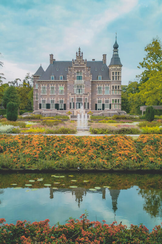 Historic mansion with a turret, surrounded by vibrant flower gardens and a reflecting pond.