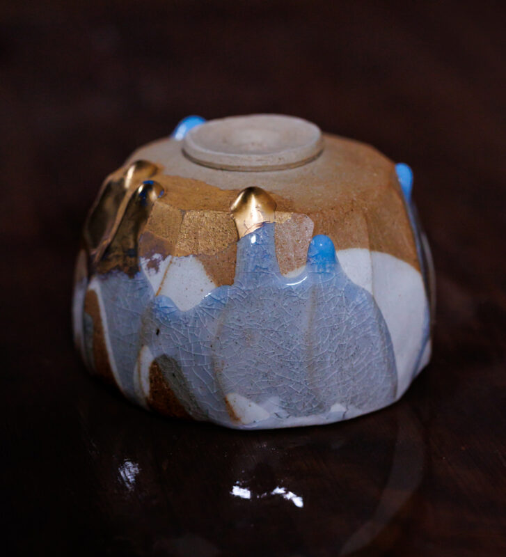 Ceramic bowl with a textured surface, featuring blue and gold accents, resting on a dark reflective surface.