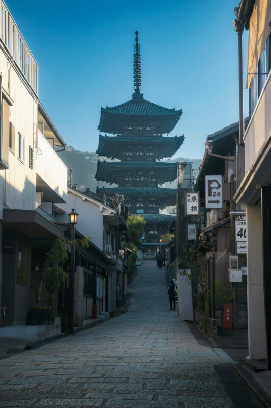 Historic pagoda towers over a narrow street lined with traditional buildings in a serene setting.