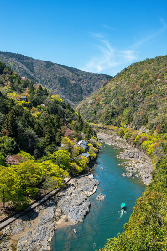 Lush green hills frame a winding river with a small boat, under a clear blue sky.
