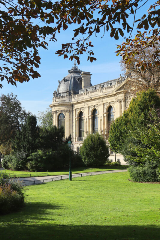 Historic building with ornate architecture surrounded by lush greenery and trees under a clear blue sky.