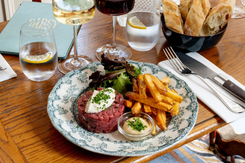 Beef tartare with herbs and sauce, served with fries, water, wine, and bread in a Parisian restaurant setting.