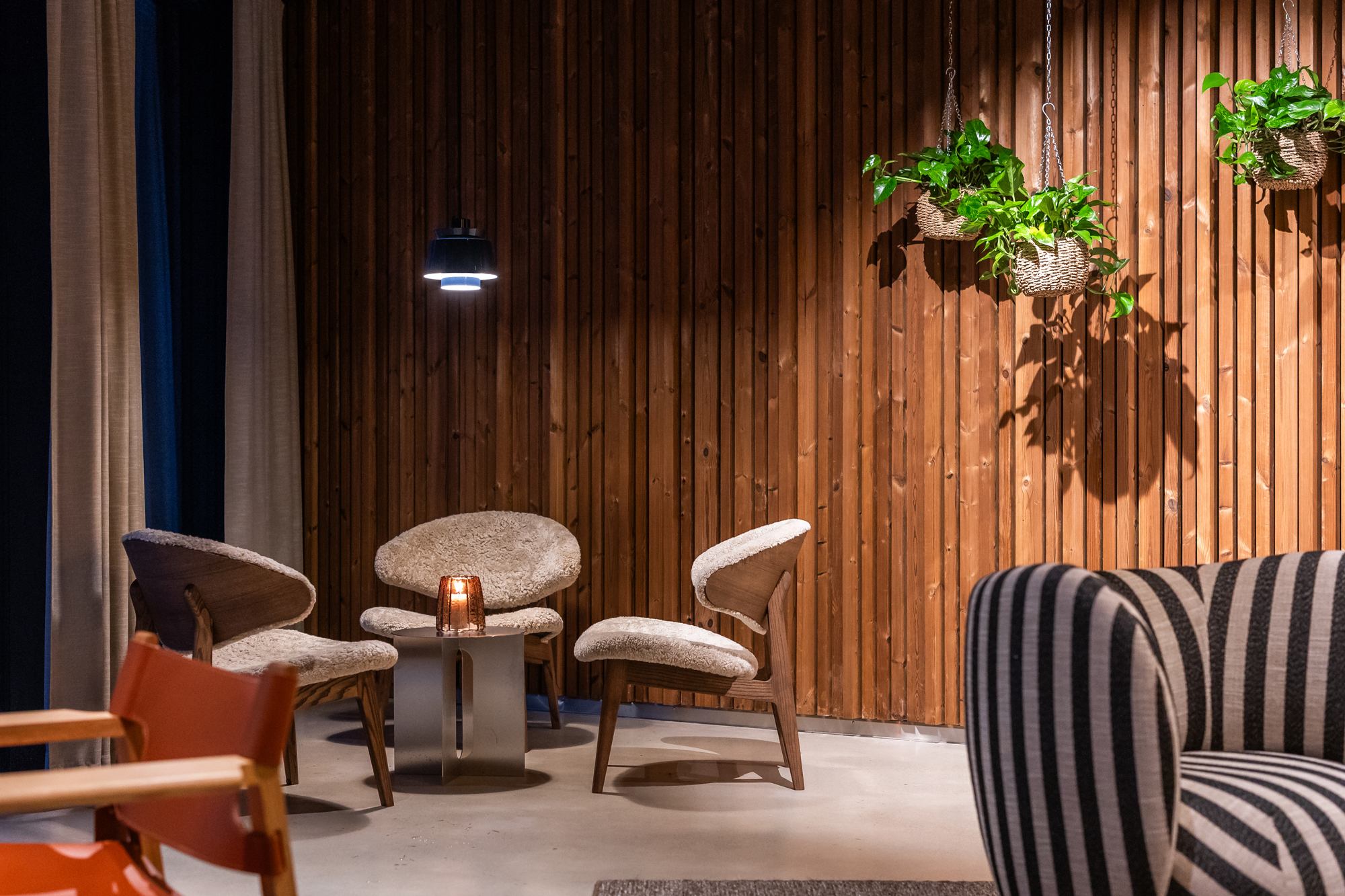 Cozy seating area with two upholstered chairs and a small table, against a wooden wall with hanging plants.