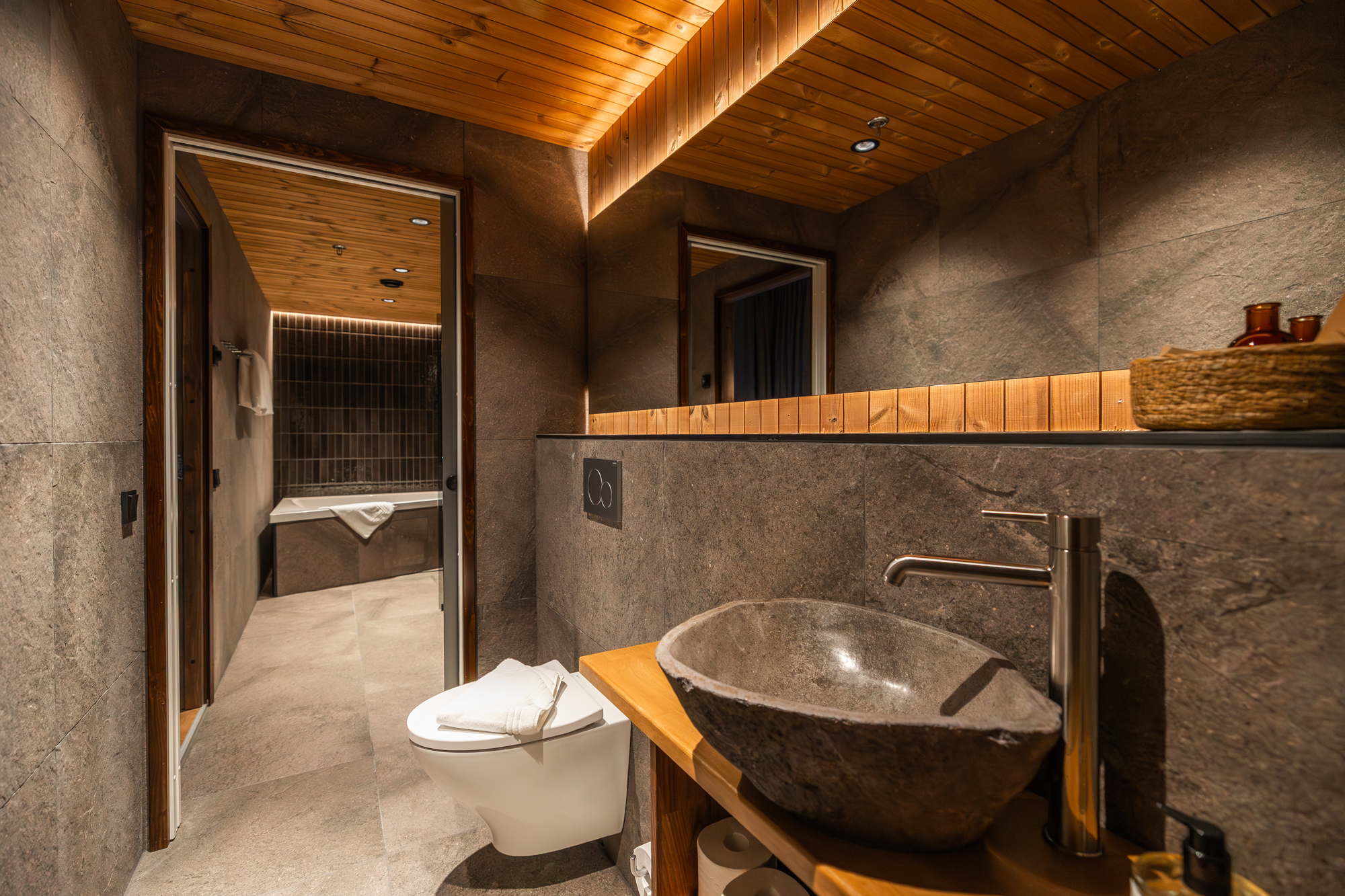 Modern bathroom featuring a stone sink, wooden accents, and a view into a separate bathing area.