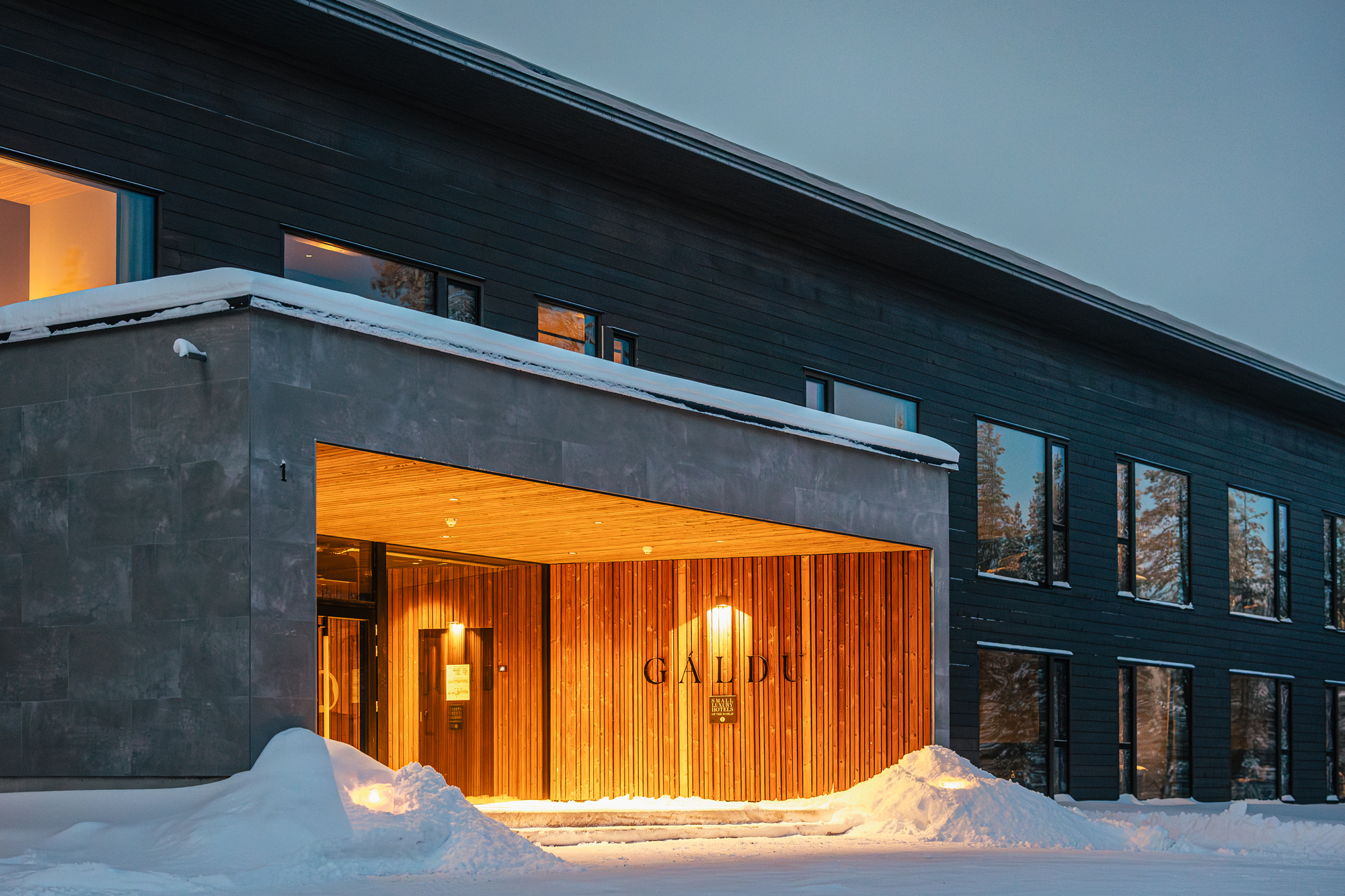 Modern hotel entrance with wooden accents, snow-covered ground, and large windows, located at Gáldu Hotel & Spa.