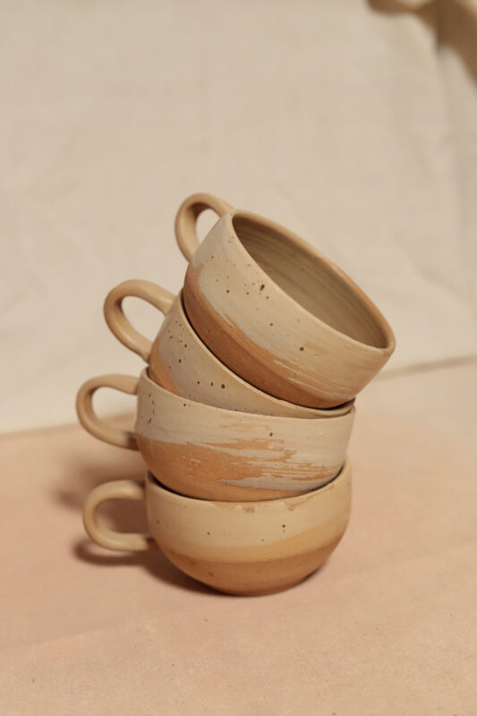 Stacked ceramic cups in earthy tones, arranged with handles facing outward against a soft, neutral background.