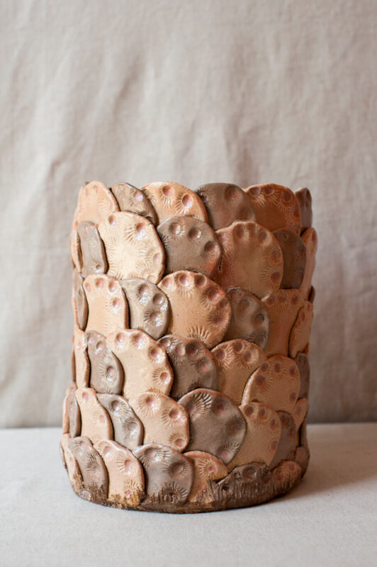 Ceramic vase with a textured surface featuring overlapping, rounded shapes in earthy tones of beige and brown.