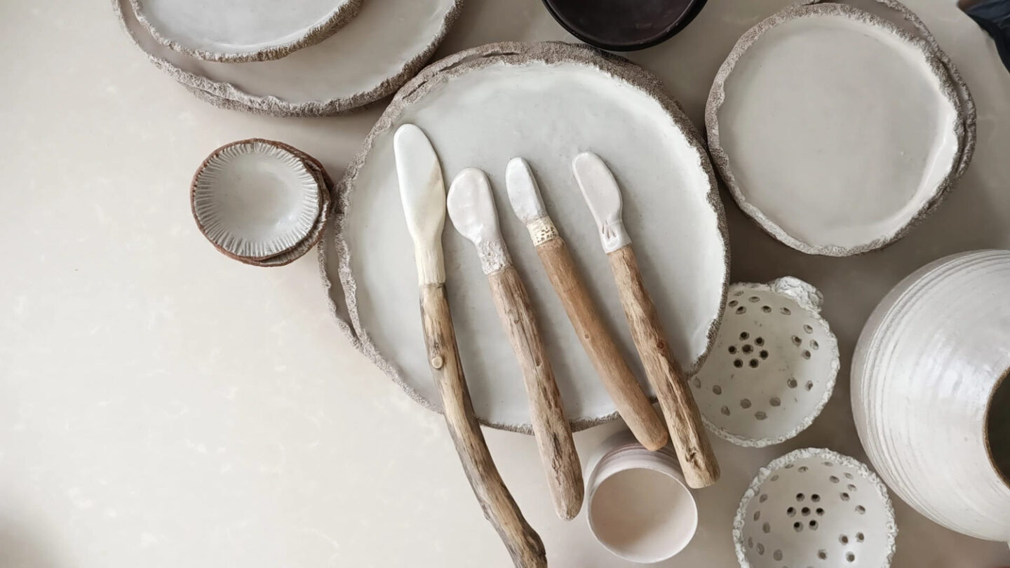 Ceramic plates and bowls arranged on a surface, featuring wooden-handled knives on a textured plate.