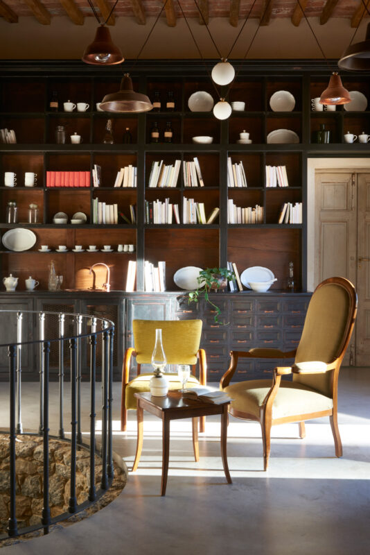 Bright living room featuring a wooden bookshelf filled with books and dishes, two chairs, and a round table.