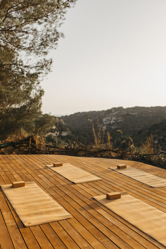 Yoga mats and blocks arranged on a wooden deck overlooking a scenic hillside at sunset.