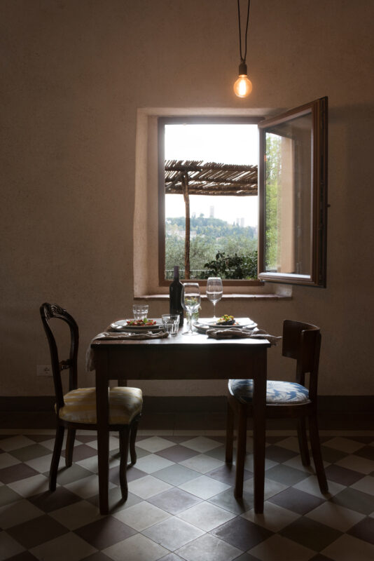 Table set for dining with glasses and a bottle, framed by an open window overlooking a scenic view.