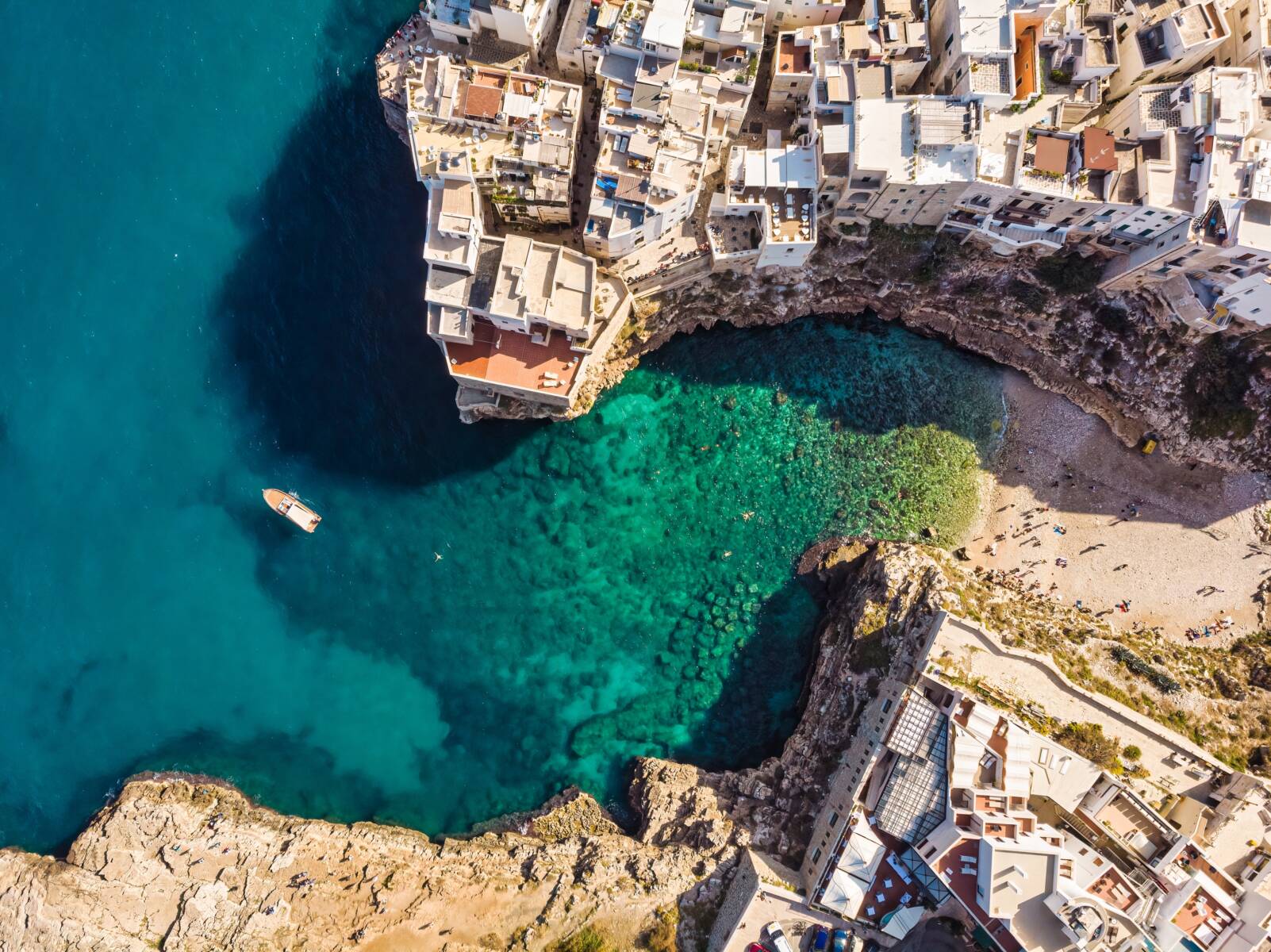Aerial view of a coastal town with white buildings, clear turquoise water, and a small beach.