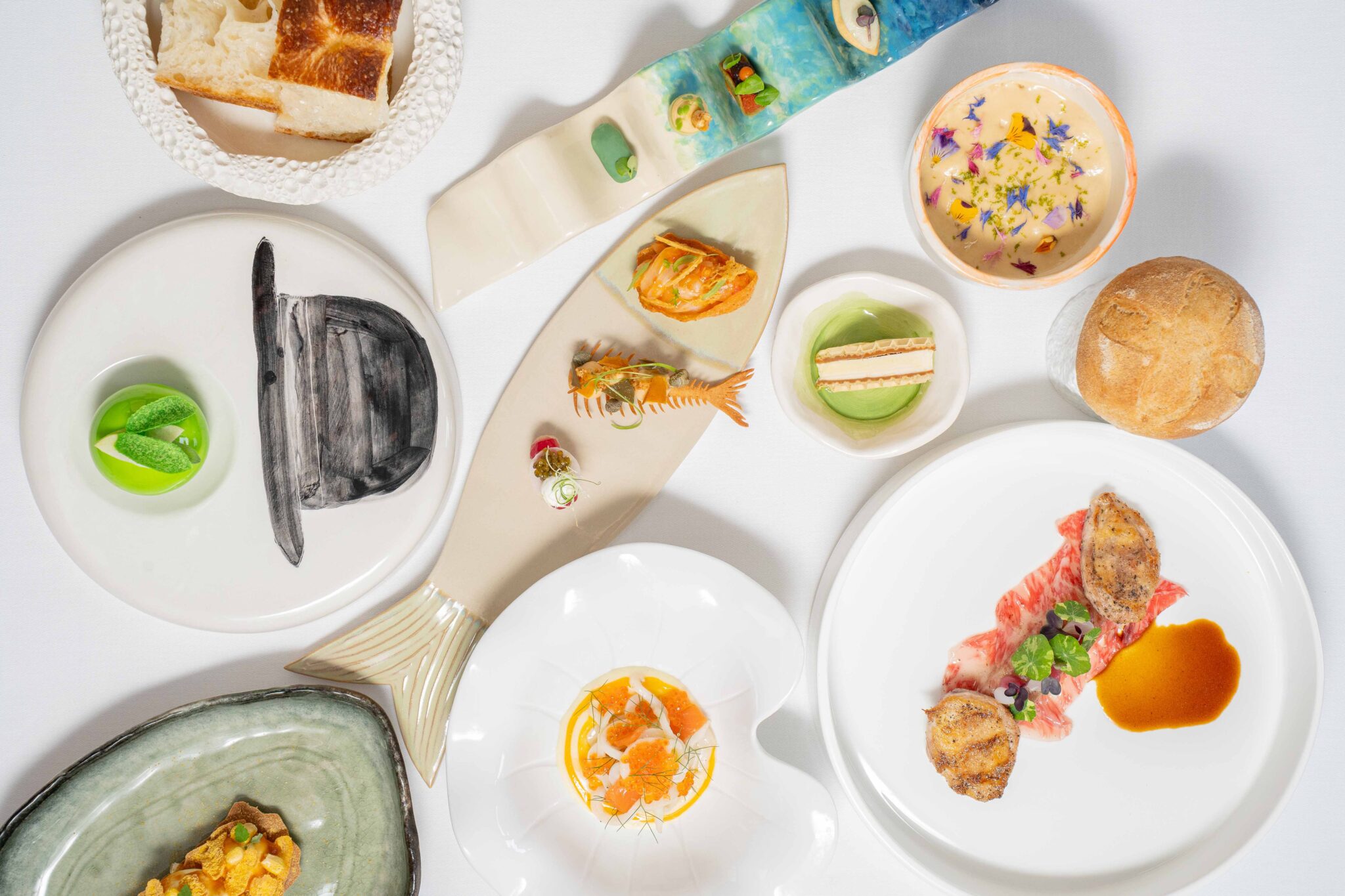 An artistic arrangement of a gourmet tasting menu featuring various dishes, including seafood, garnishes, and bread.
