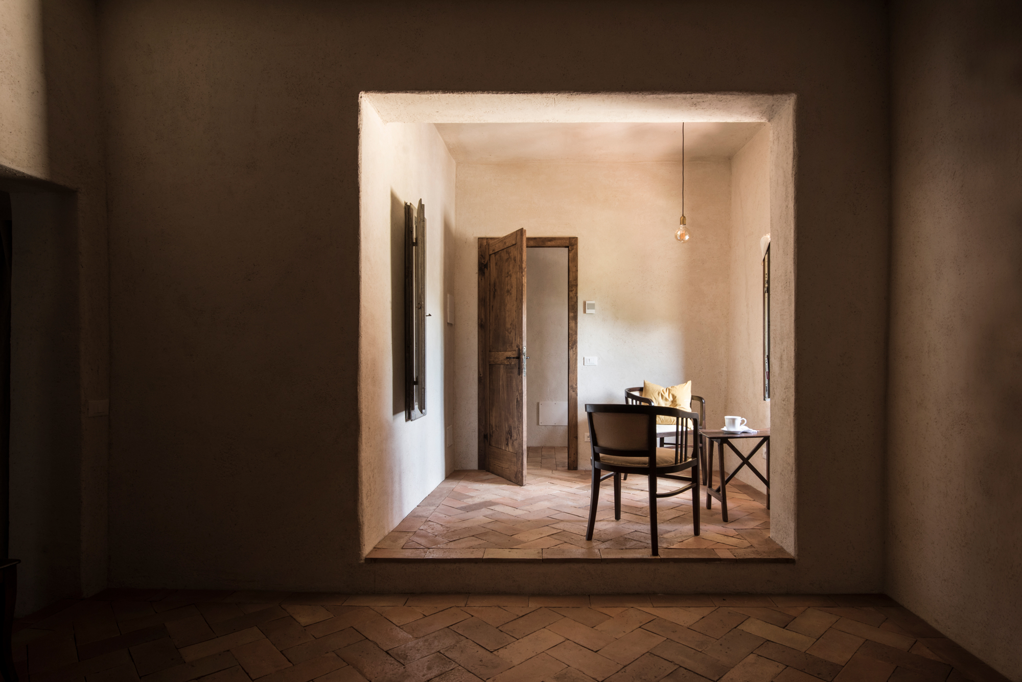 A cozy room with a wooden door partially open, featuring a small table and chairs, illuminated by a pendant light.