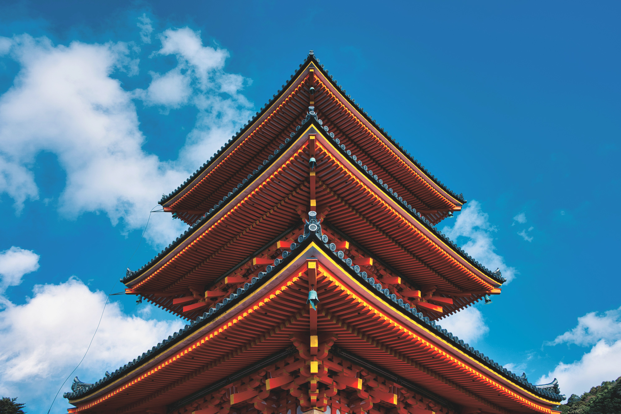 Three-tiered pagoda with ornate roofs against a bright blue sky and scattered clouds.