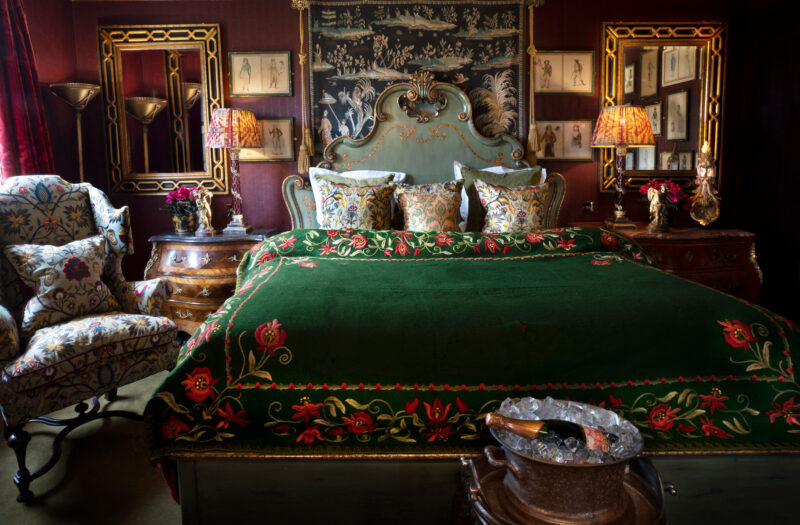 Luxurious bedroom at Prestonfield House featuring a green embroidered bedspread, floral pillows, ornate mirrors, and elega...