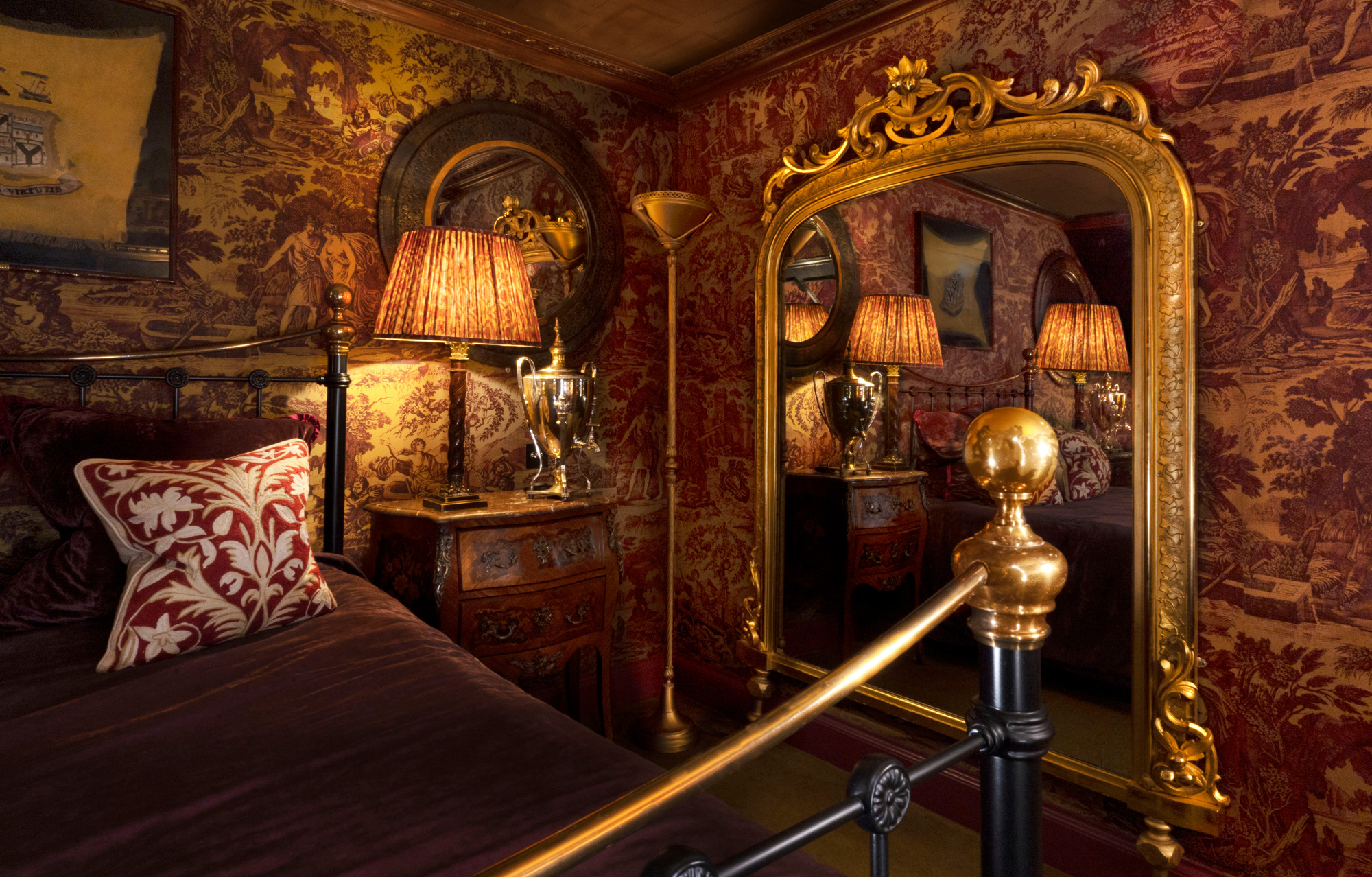 Luxurious bedroom in Prestonfield House featuring ornate wallpaper, a gilded mirror, and elegant lighting.