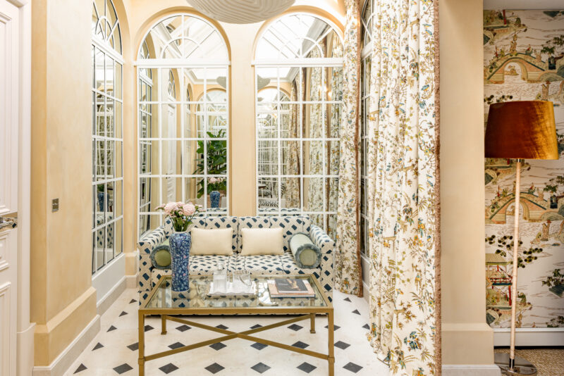 Lounge area of the Top Floor Junior Suite at Saint James Paris, featuring a patterned sofa, glass table, and floral curtains.