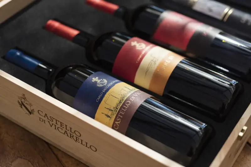 Four wine bottles with colorful labels, displayed in a wooden box branded "Castello di Vicarello.