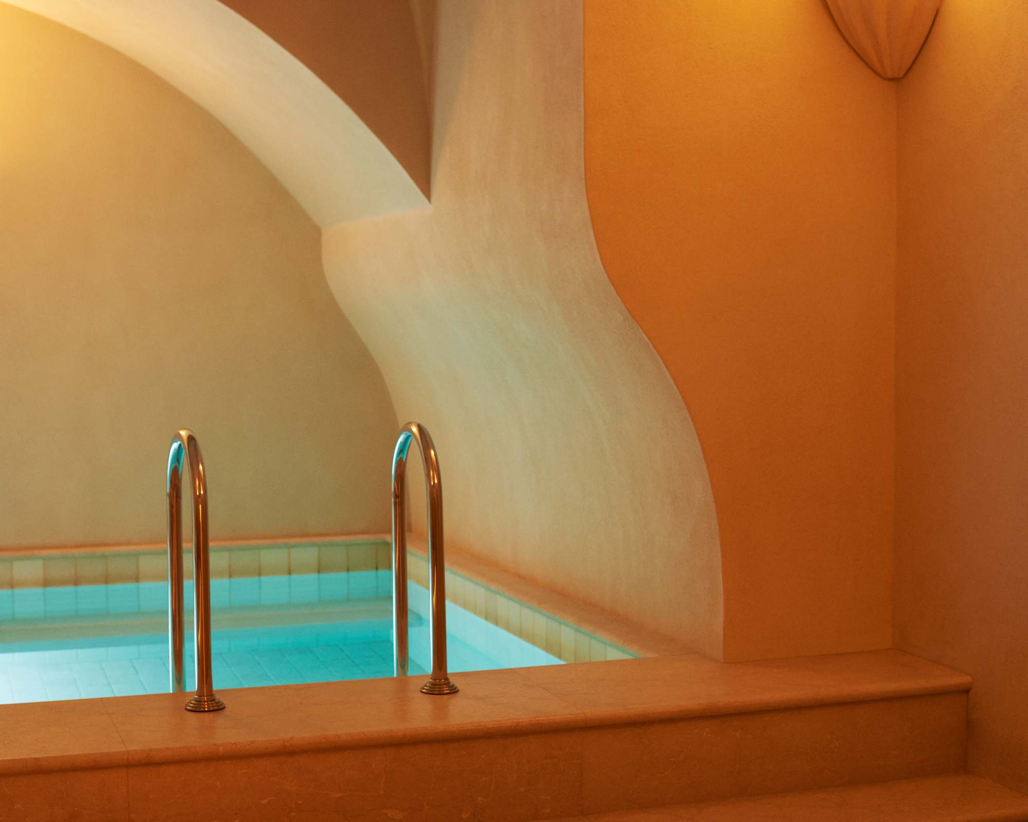 Indoor swimming pool with curved walls and steps, softly lit with warm tones.