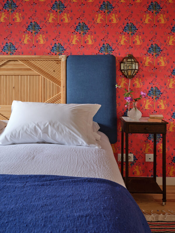 Cozy bedroom featuring a bed with white pillows, a blue throw, and vibrant red wallpaper with floral and animal patterns.