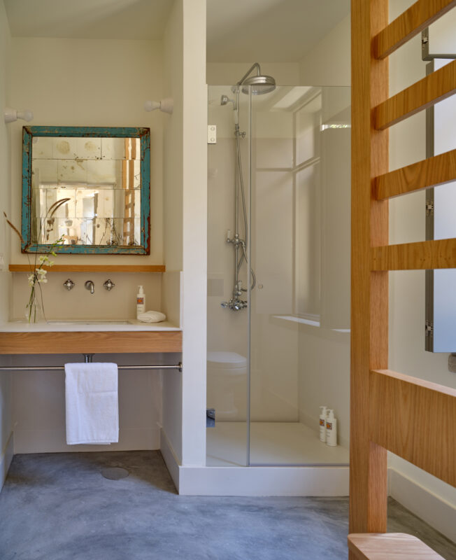 Modern bathroom with a shower, wooden accents, a mirror, and toiletries, featuring a minimalist design.