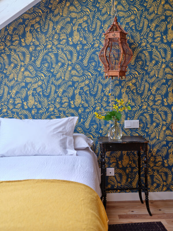 Cozy bedroom featuring a white bed with yellow blanket, a patterned blue wall, and a wooden lantern hanging above a side t...