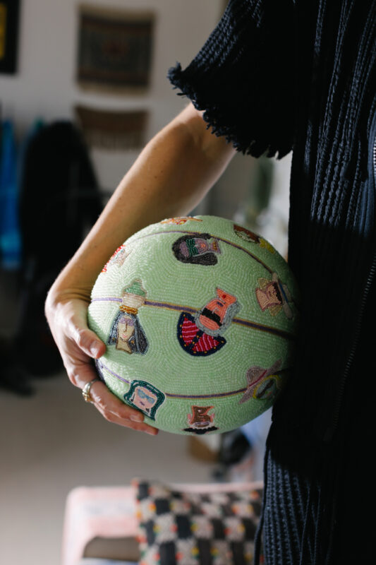 A person holds a decorative green basketball adorned with colorful, illustrated faces and patterns.