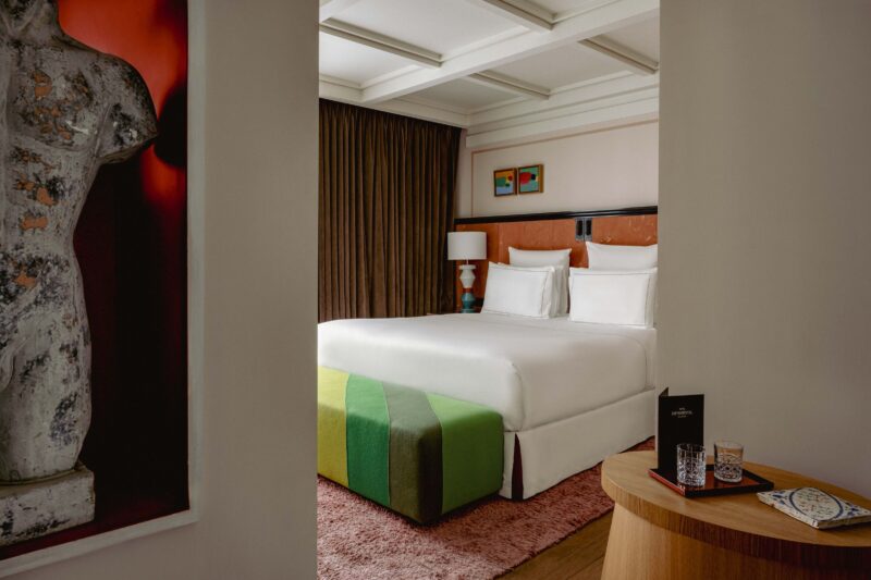 Modern hotel room featuring a white bed with green accents, a wooden table, and artwork on the walls.