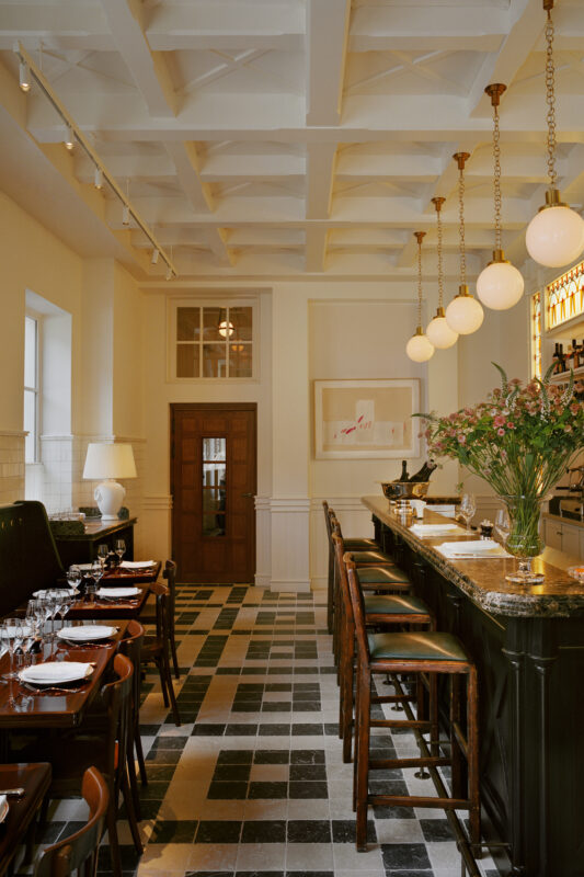 Elegant restaurant interior featuring a bar with pendant lights, floral centerpiece, and checkered floor.