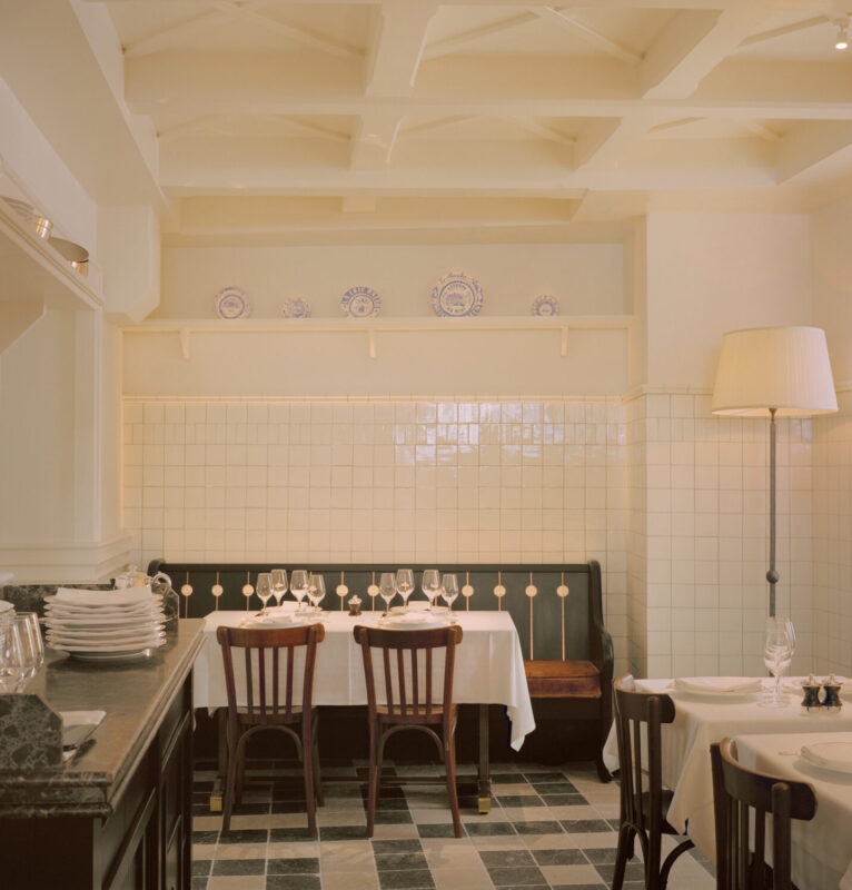 Elegant dining area with white tablecloths, wooden chairs, and decorative plates on the wall at Château Voltaire.