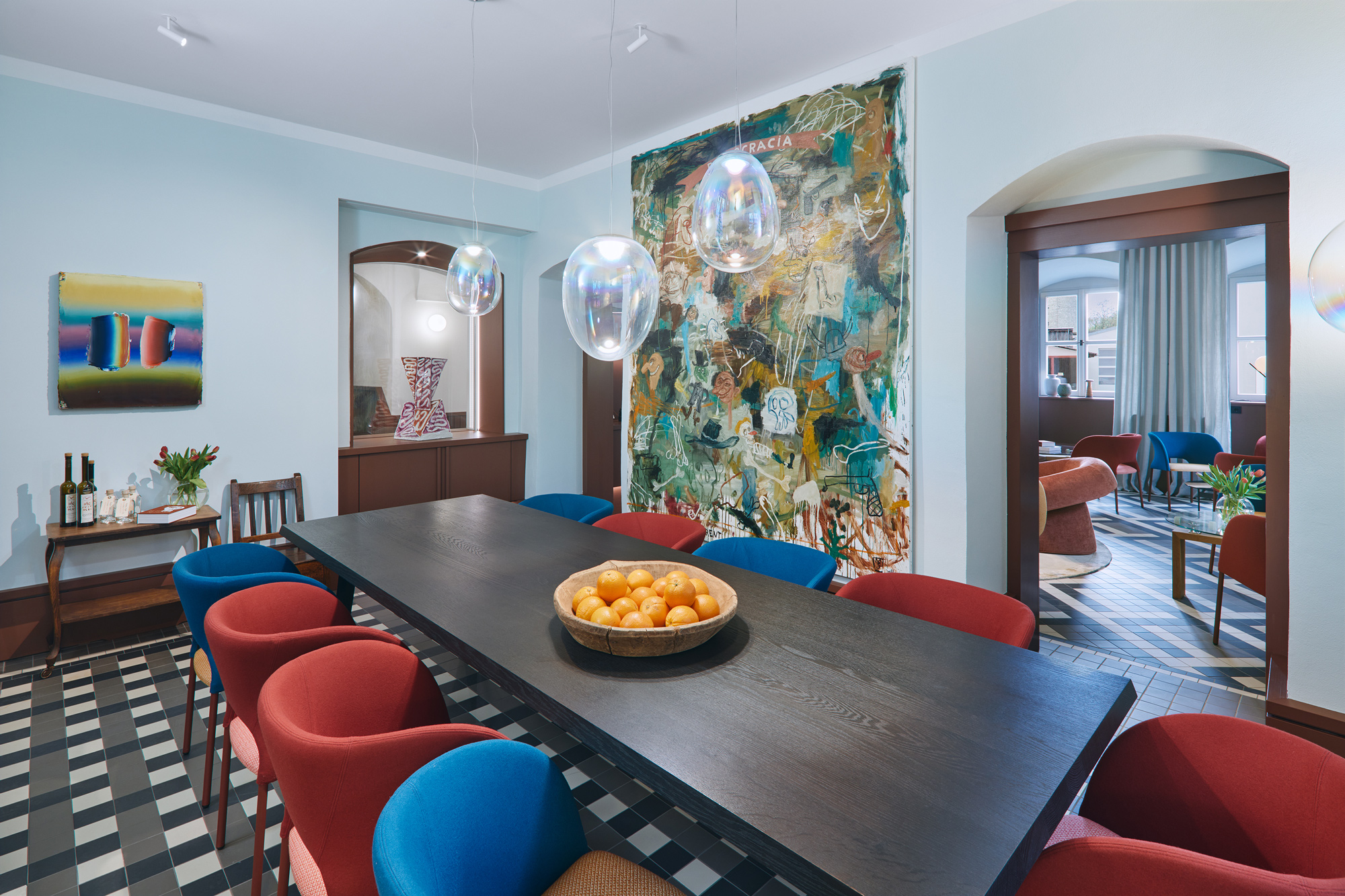 Modern dining area in Engelwirt Hotel featuring a long dark table, colorful chairs, and a large artwork on the wall.
