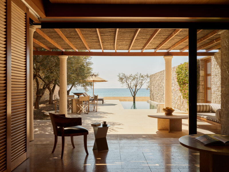 View from a beach pavilion terrace at Amanzoe, featuring a pool, outdoor dining area, and sea in the background.