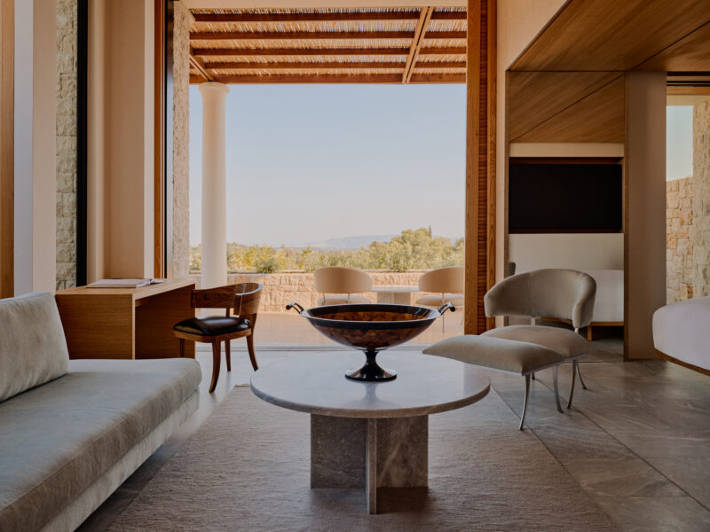 Modern interior of a villa at Amanzoe, featuring a stone table, plush seating, and a view of the landscape through large w...