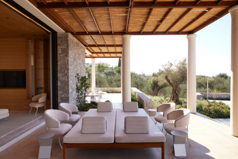 Modern outdoor seating area with plush sofas and small tables, surrounded by greenery at Amanzoe, Greece.